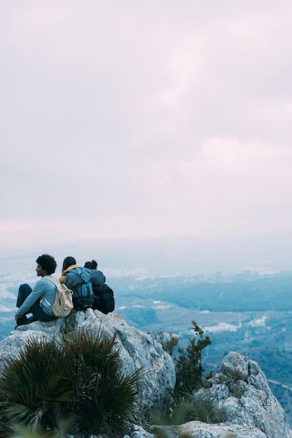 Image of three students sitting on a mountain, enjoying the view with backpacks