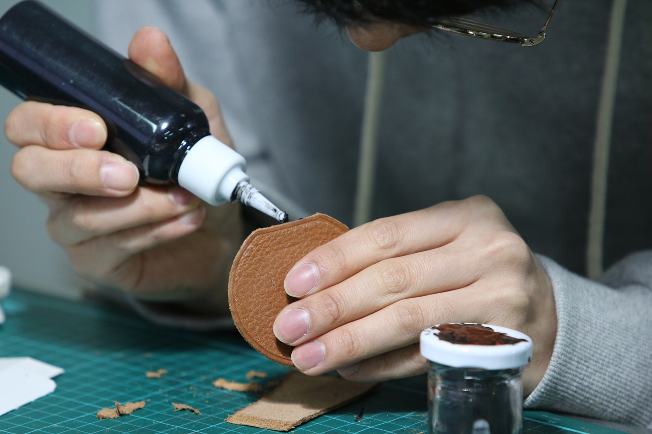 A craftsman working with leather, using glue and tools to handcraft a leather piece, emphasizing the traditional crafting techniques.