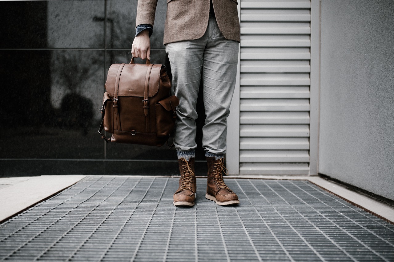 A man in a blazer holding a handcrafted leather bag, standing on a city street with stylish boots, perfect for a gift for him